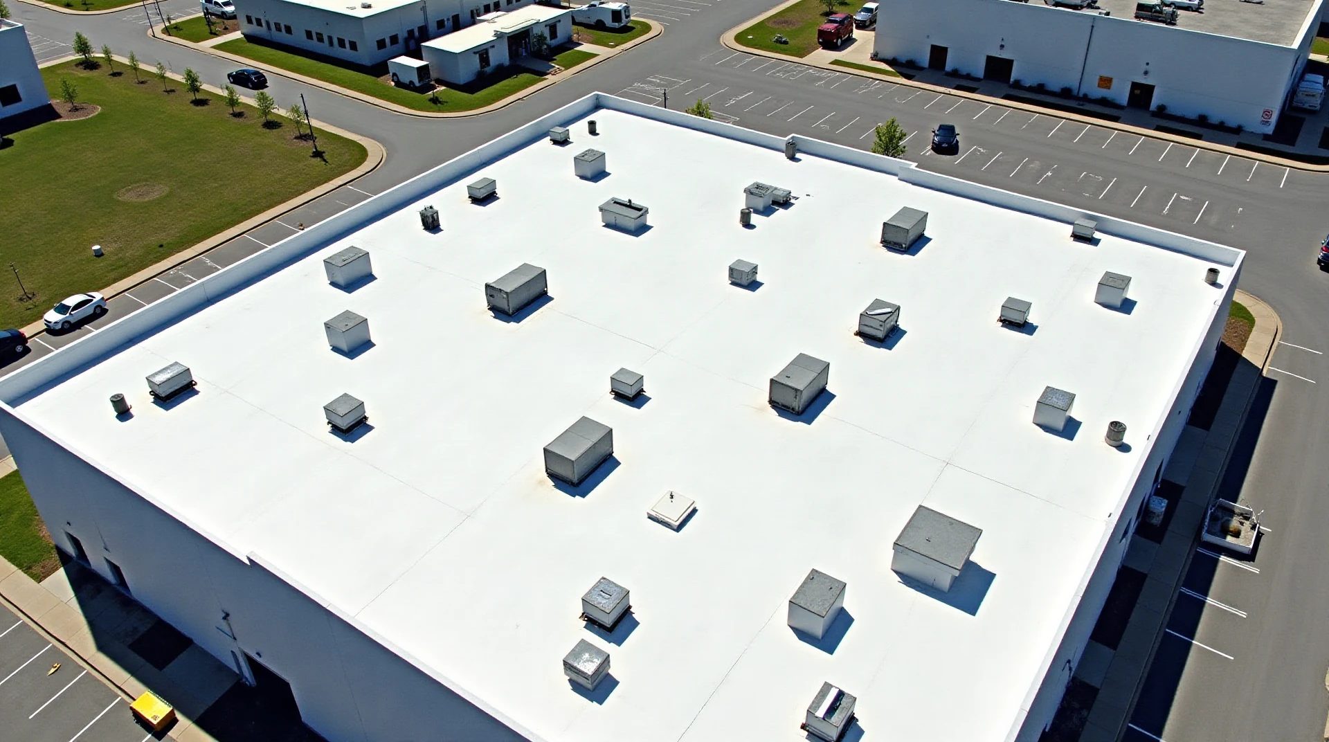 Aerial view of a vast low-slope commercial roof on a large modern building with rooftop units and clean new membrane seams, bright daylight